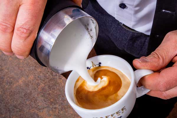 Barista Jens Kirmse gießt cremig aufgeschäumte Milch für Latte Art in eine Kaffeetasse