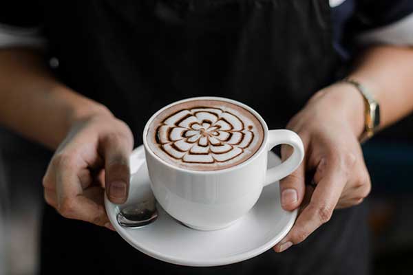 Barista hält eine weiße Tasse frischen Caffè Mocha mit kunstvoller Latte Art